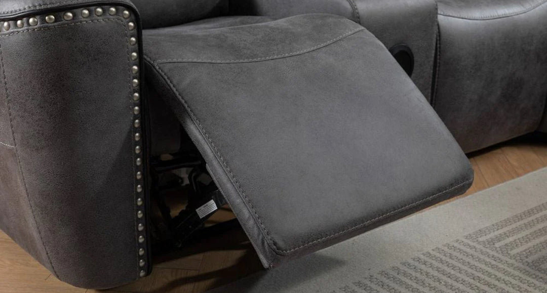 Close-up of grey reclining sofa footrest with nailhead trim, showcasing extended leg support on wooden flooring