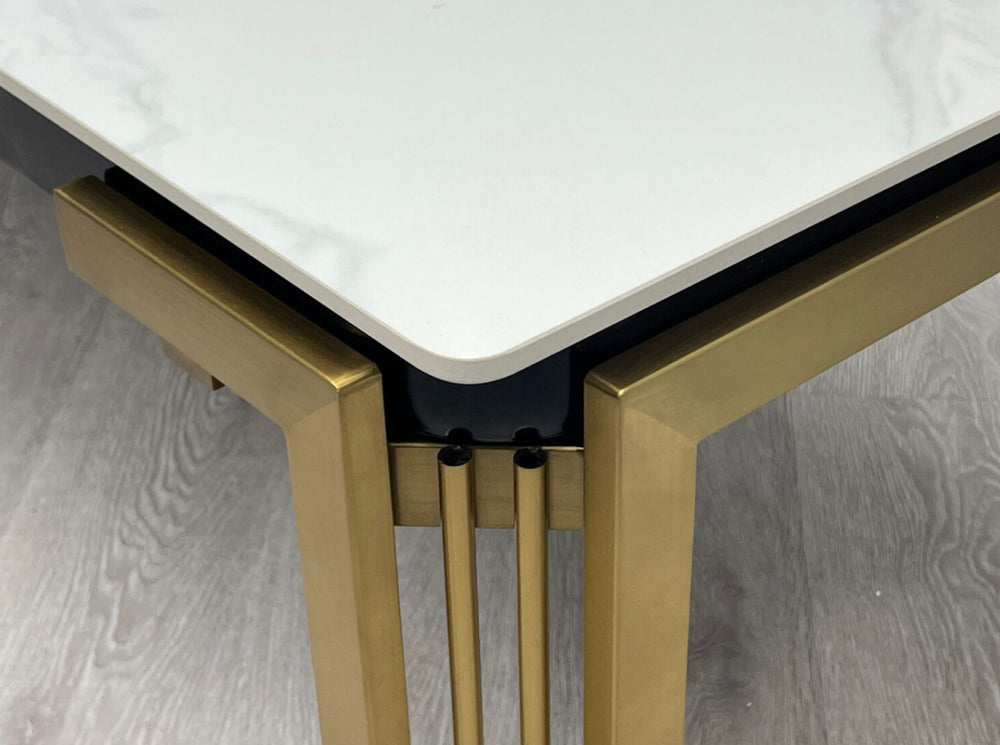 A white ceramic coffee table with a gold frame and gold accents on a grey floor, with a marble-like appearance on the tabletop.