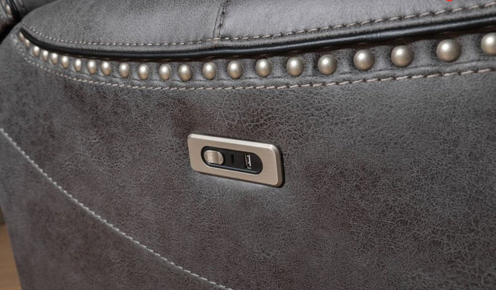 Close-up of grey leather reclining sofa with built-in USB charging port and nailhead trim detailing