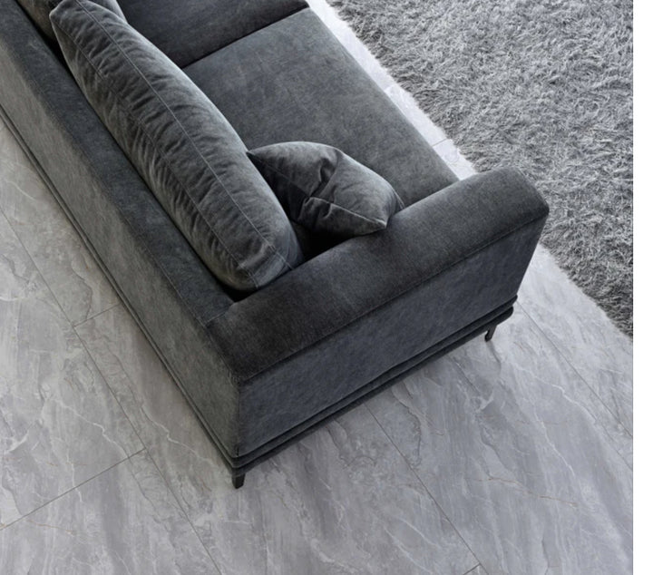 Close-up of dark grey velvet sofa armrest with plush cushions and black metal legs on a soft grey shaggy rug