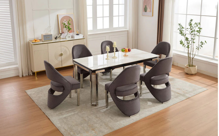 A white marble dining table with silver legs accompanied by grey upholstered dining chairs in a room with light decor.