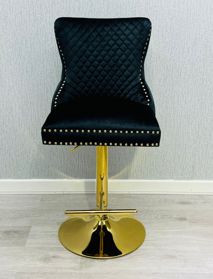 A black colored bar stool with gold accents, featuring a tufted backrest and a lion knocker on the back.
