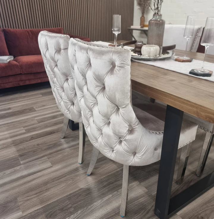 Two beige velvet Kensington dining chairs with chrome legs and deep buttoned back design, pictured in a room setting with a wooden dining table.