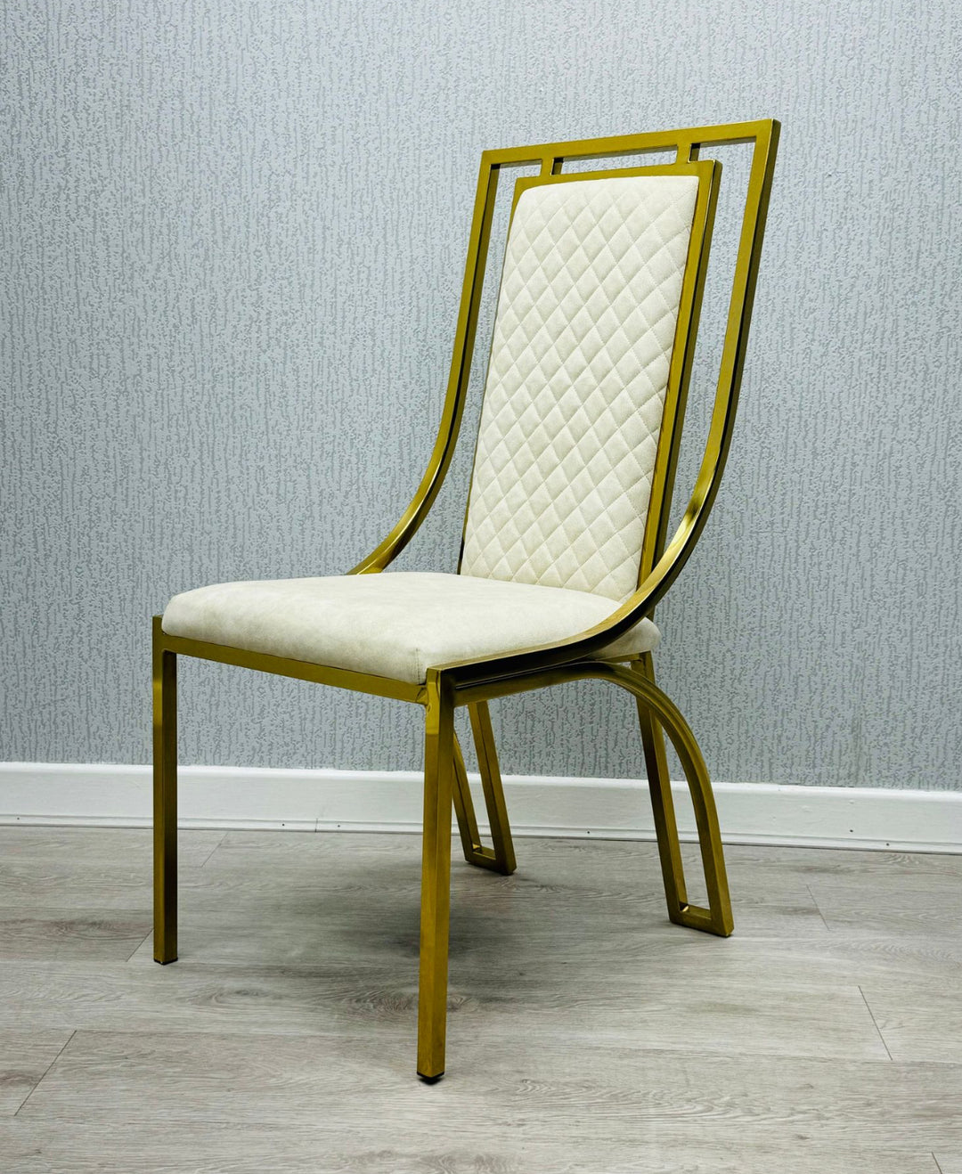 single  modern high back dining chairs with quilted cream upholstery and gold stainless steel frame, shown on light wood flooring against textured wallpaper