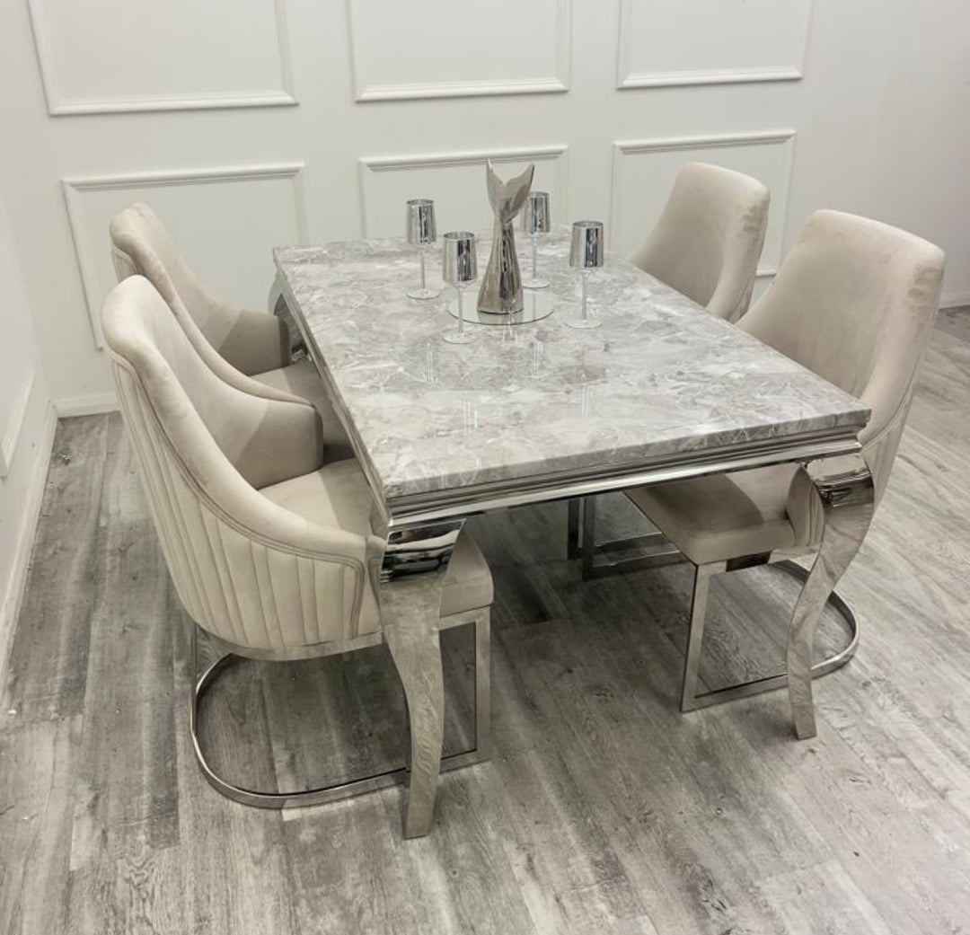 A beige marble dining table with stainless steel legs, accompanied by four upholstered dining chairs in a room with gray flooring.