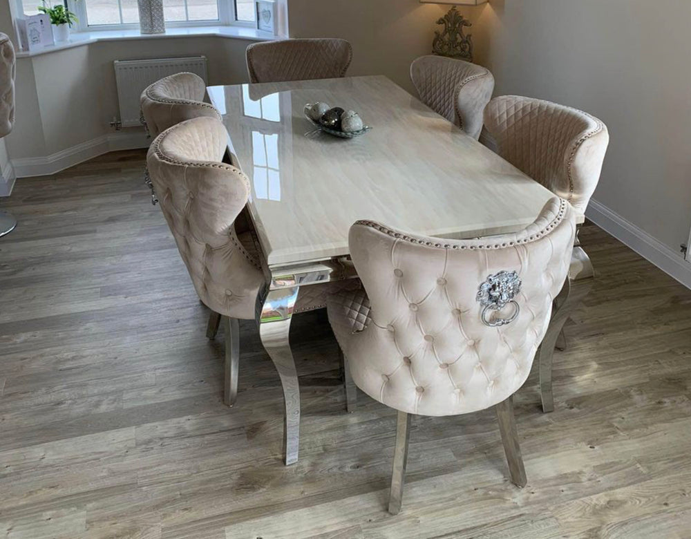 A square marble dining table with cream color upholstered chairs with tufted backrests and lion knocker designs on the headrests.