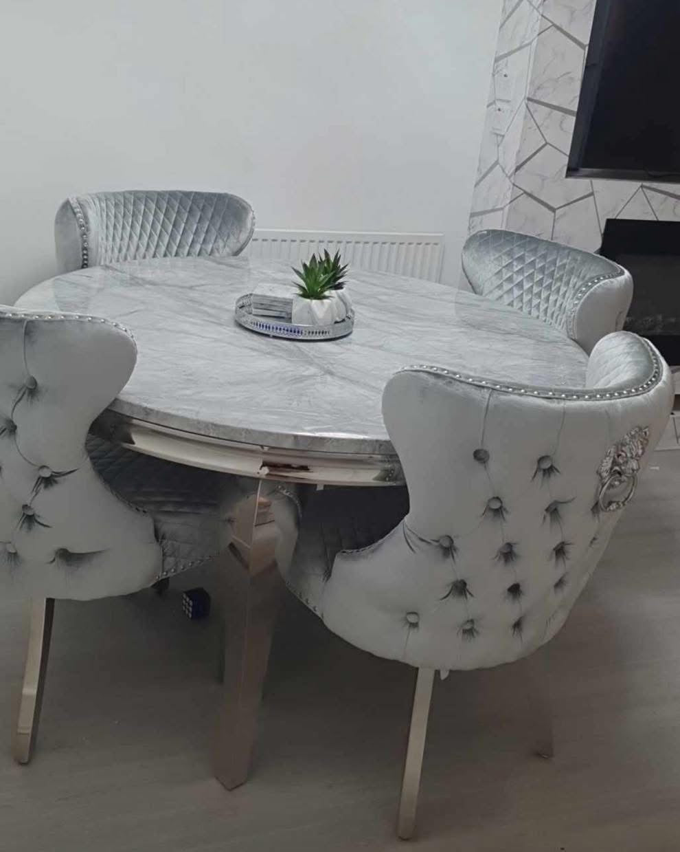 A round dining table with a grey marble-like finish accompanied by four upholstered dining chairs with a tufted design and silver accents on the legs.