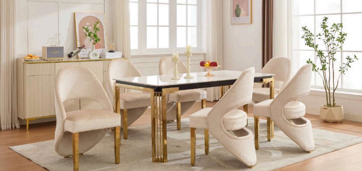A white and gold dining table with cream and gold chairs arranged around it in a room with a light interior.
