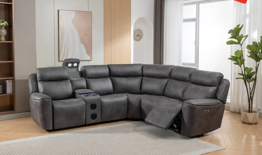 A gray fabric corner recliner sofa with multiple seats and an electronic control panel, situated in a room with a light-colored wall and a potted plant in the background.