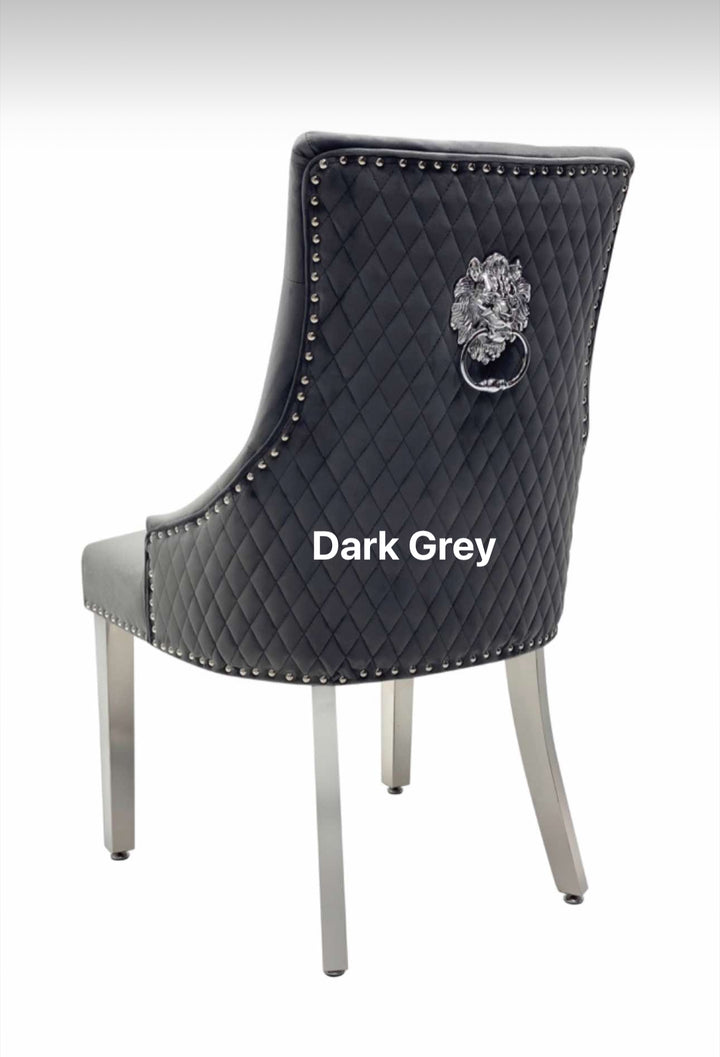 A beige upholstered dining chair with a dark grey lion knocker on the backrest and chrome-colored legs.