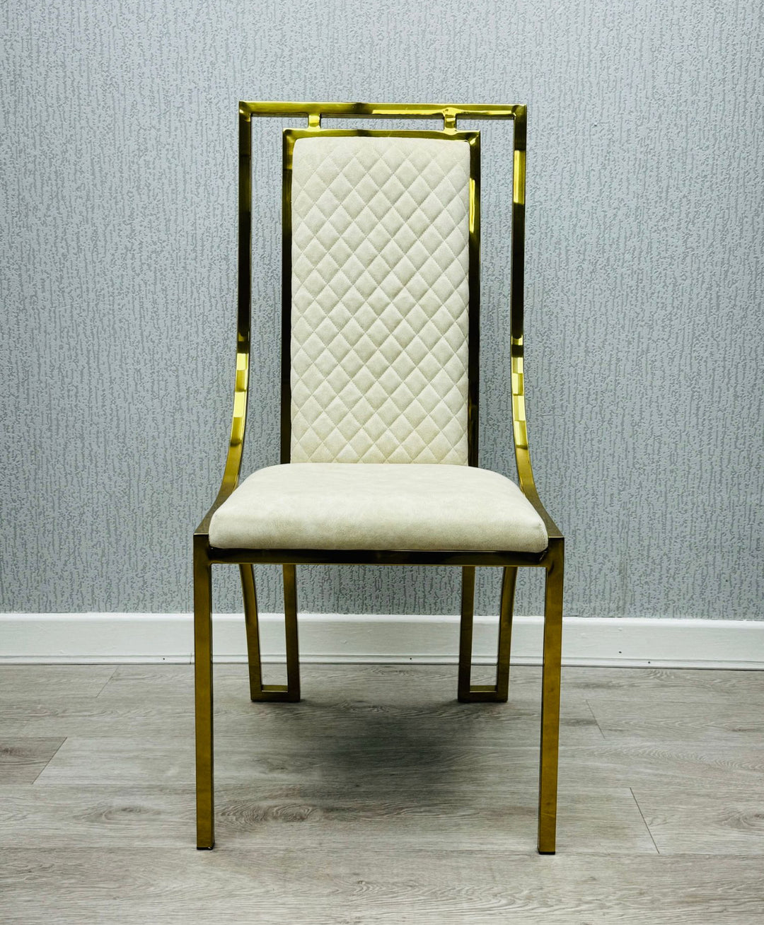 single  modern high back dining chairs with quilted cream upholstery and gold stainless steel frame, shown on light wood flooring against textured wallpaper