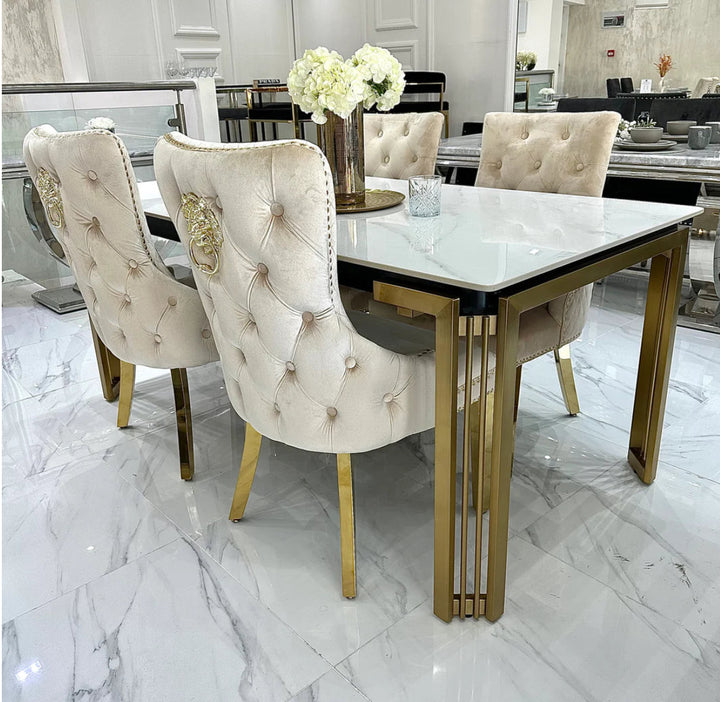 A white marble dining table with gold legs, accompanied by beige upholstered dining chairs with gold accents.