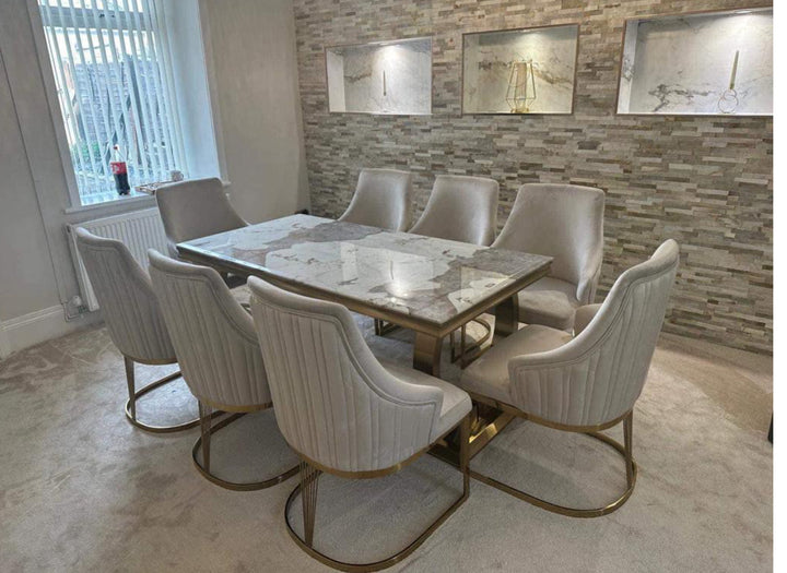 Luxury marble dining table set with eight cream velvet chairs featuring gold metal legs, placed in a modern dining room with feature stone accent wall