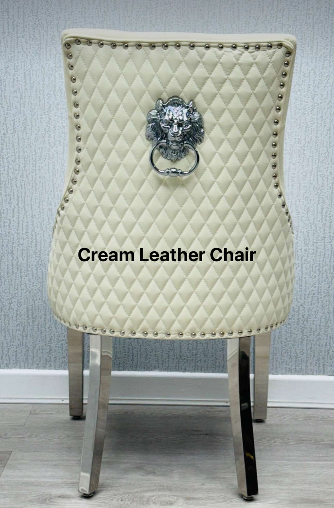 A beige upholstered dining chair with a light grey lion knocker on the backrest and chrome-colored legs.