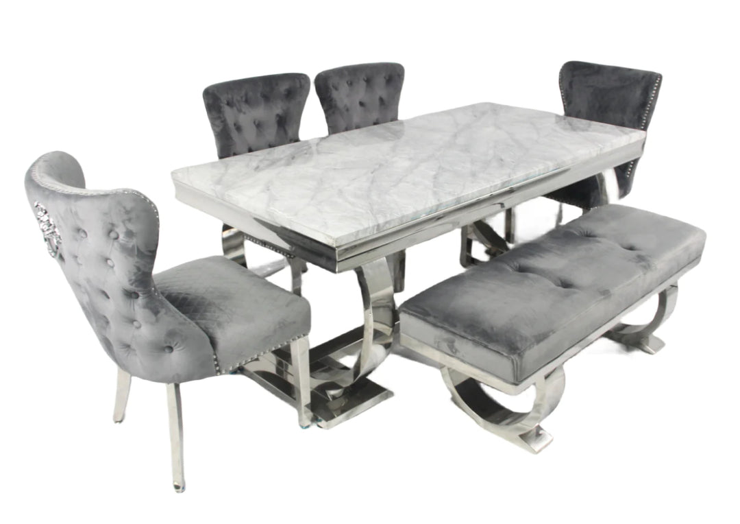 A marble dining table with a rectangular shape and four dark grey leather chairs with upholstered seats and backrests, featuring a polished metallic frame.