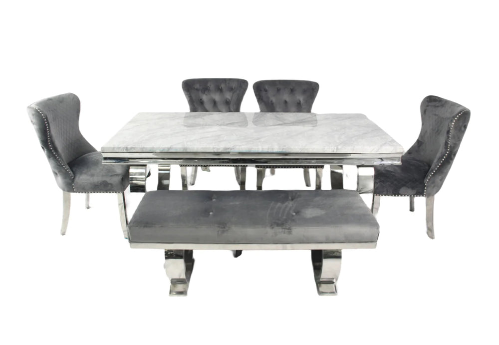 A marble dining table with a rectangular shape and four dark grey leather chairs with upholstered seats and backrests, featuring a polished metallic frame.