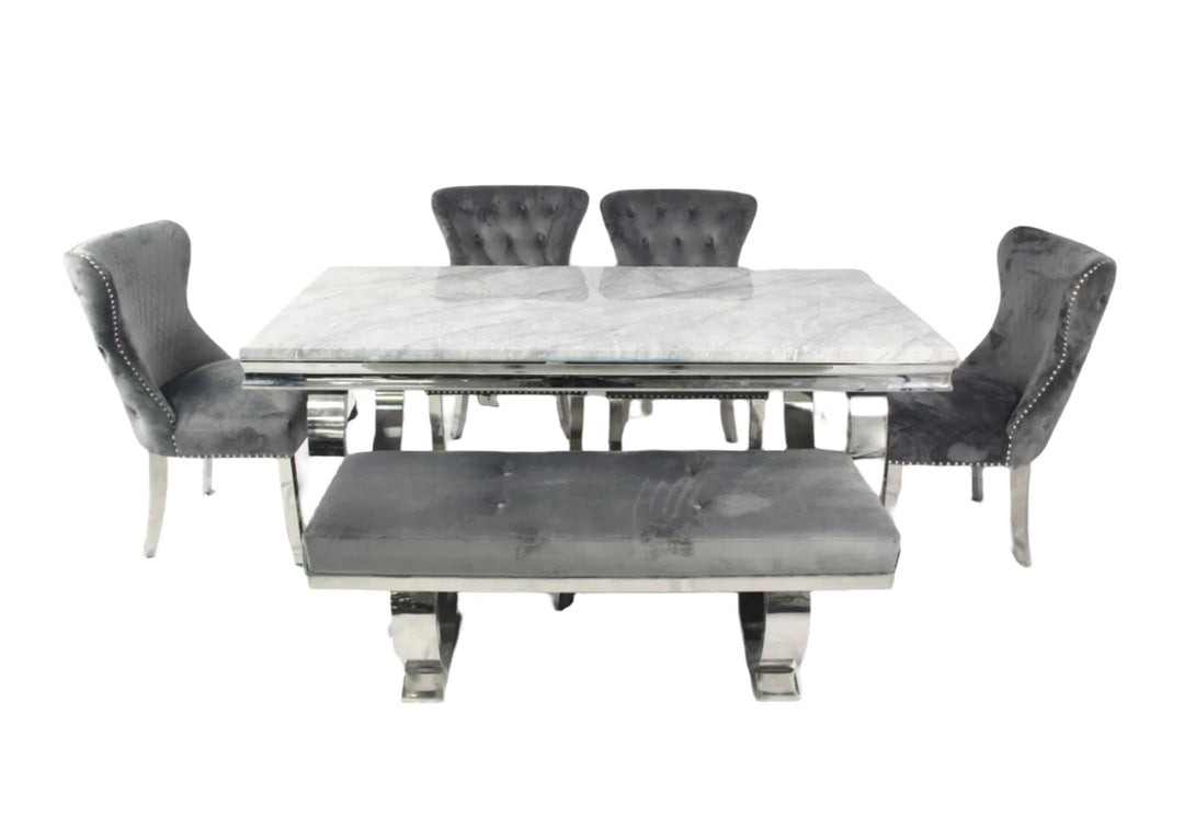 A marble dining table with a rectangular shape and four dark grey leather chairs with upholstered seats and backrests, featuring a polished metallic frame.