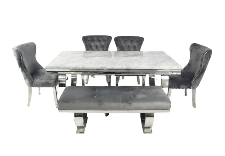 A marble dining table with a rectangular shape and four dark grey leather chairs with upholstered seats and backrests, featuring a polished metallic frame.