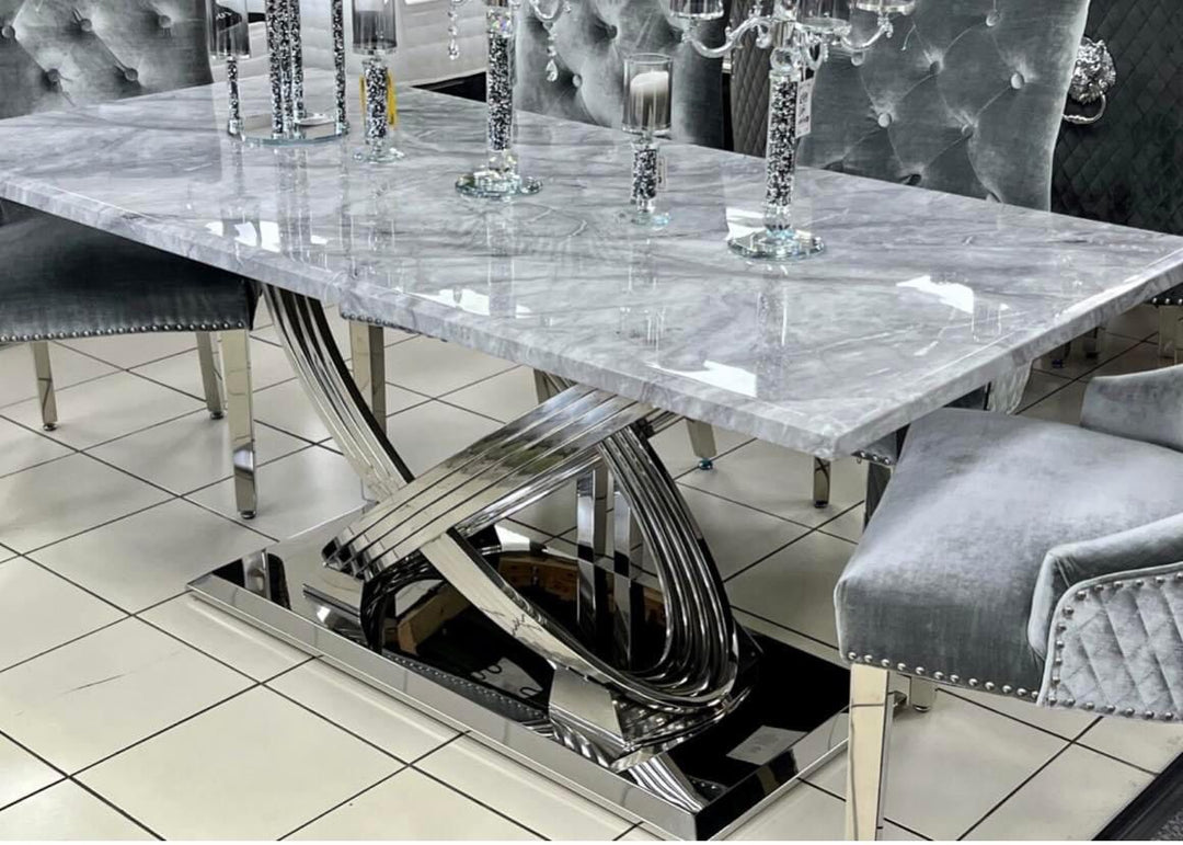A grey marble dining table with a chrome base, surrounded by chairs with grey upholstery, set on a white tiled floor.