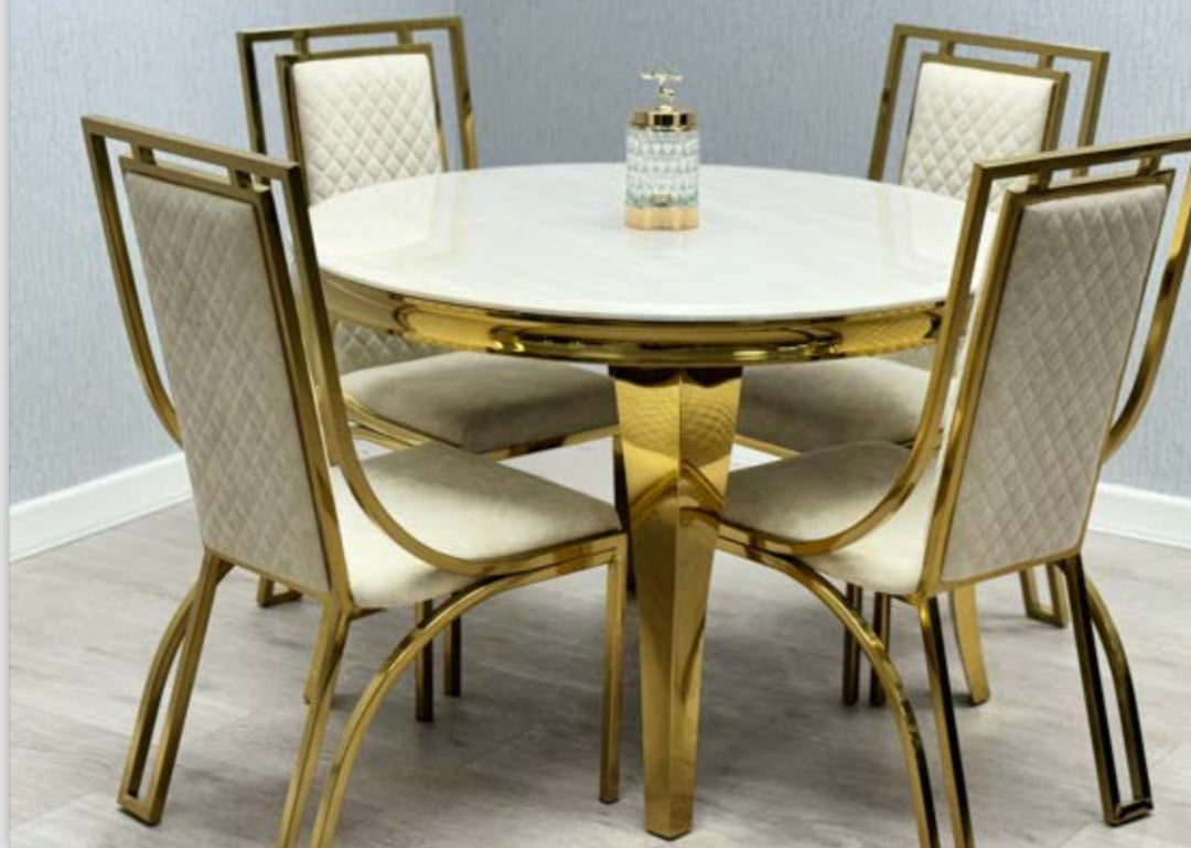 A round marble dining table in cream and gold colors, with four matching dining chairs with gold legs and cream upholstery.