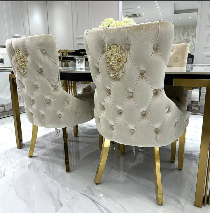 A white marble dining table with gold legs, accompanied by beige upholstered dining chairs with gold accents.