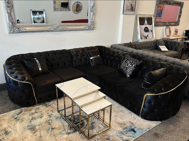A large black corner sofa with gold accents, arranged in a showroom setting with decorative cushions and a coffee table in the foreground.