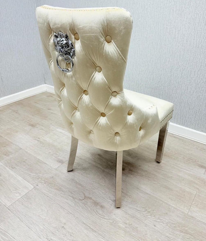 A cream-colored dining chair with a tufted backrest and a decorative lion and ring knocker on the back.