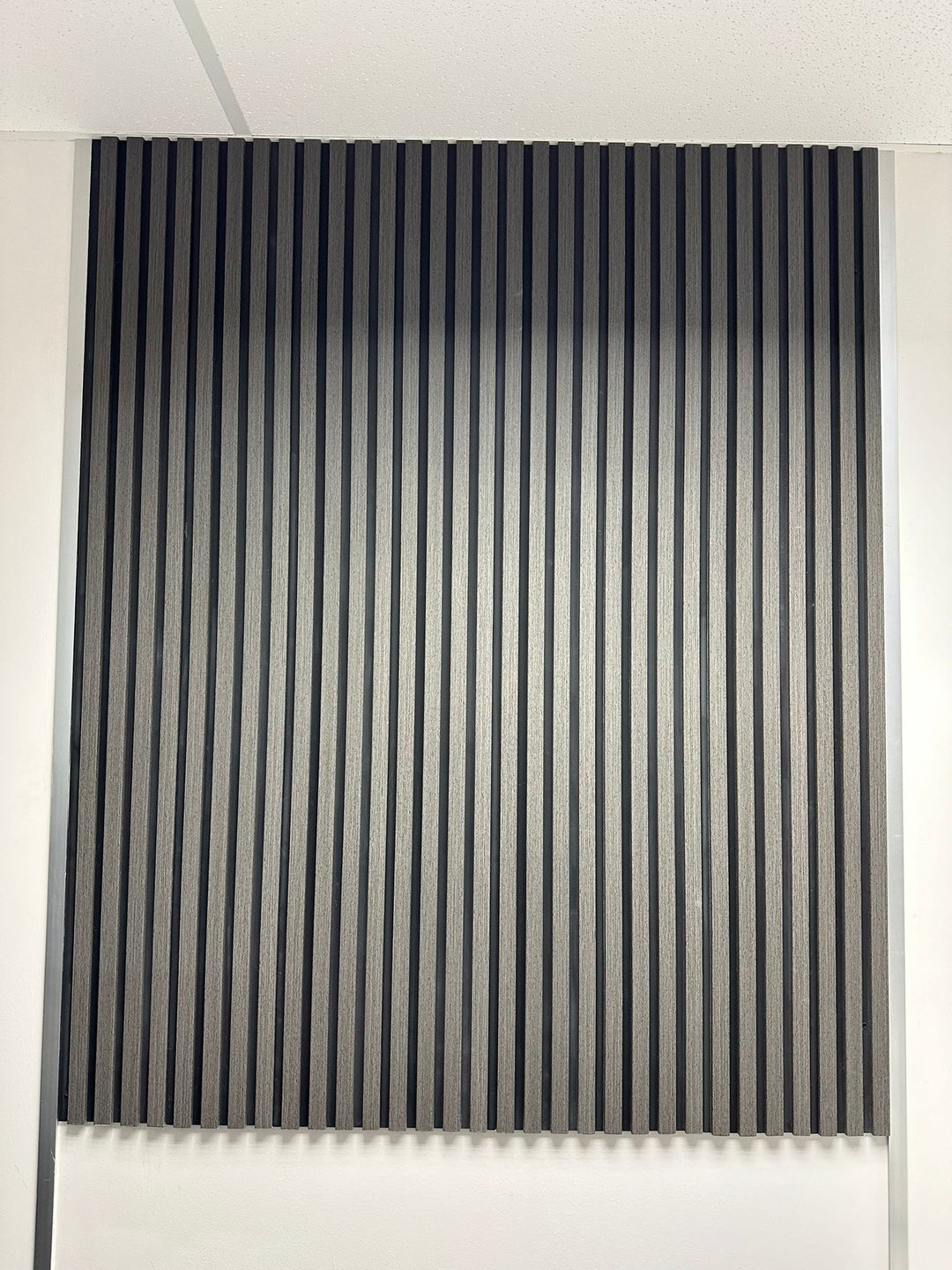 A set of wood effect veneer wall panels in an ash grey color, installed on a wall with a table and chairs in front of them.