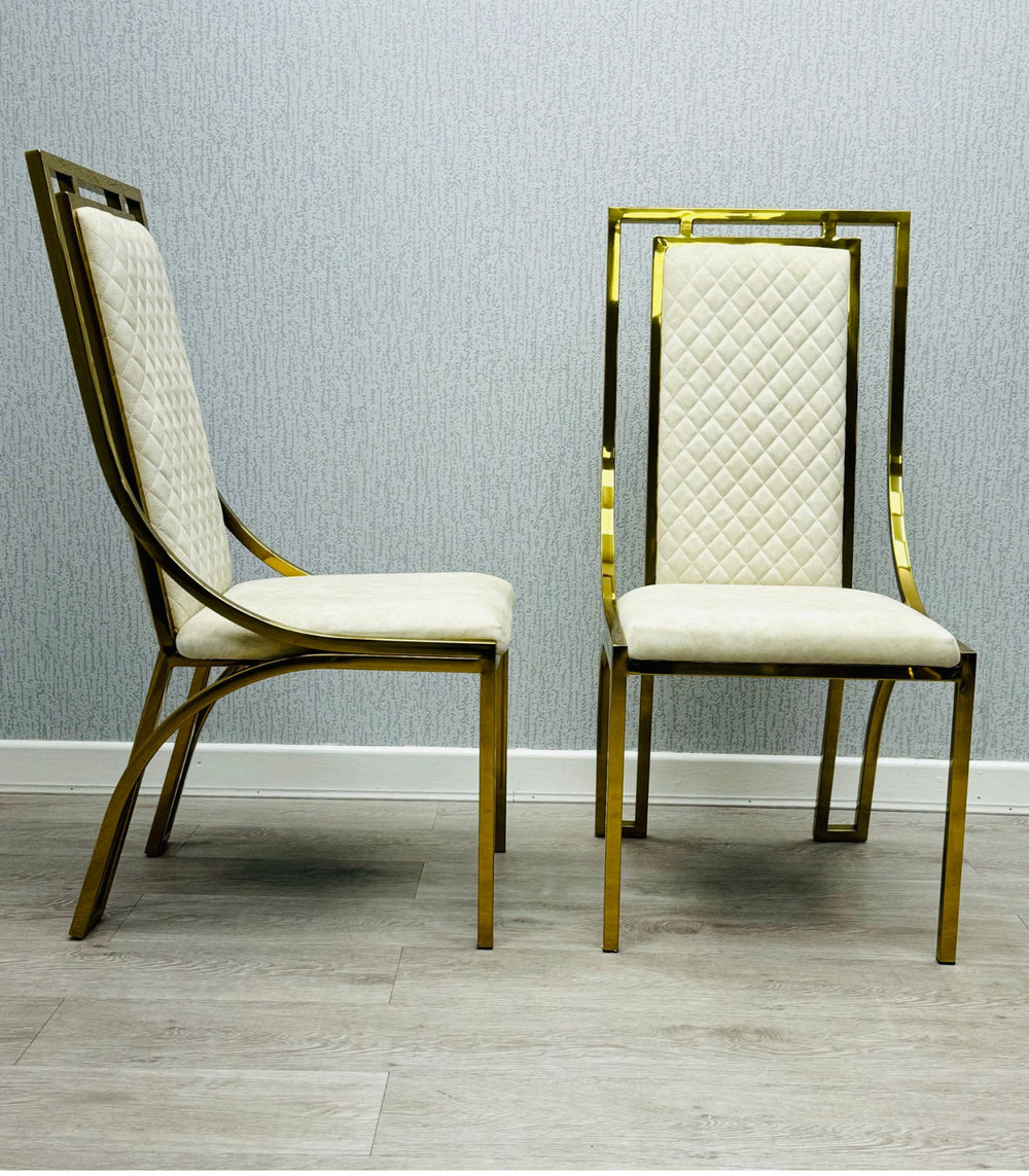 Set of modern high back dining chairs with quilted cream upholstery and gold stainless steel frame, shown on light wood flooring against textured wallpaper