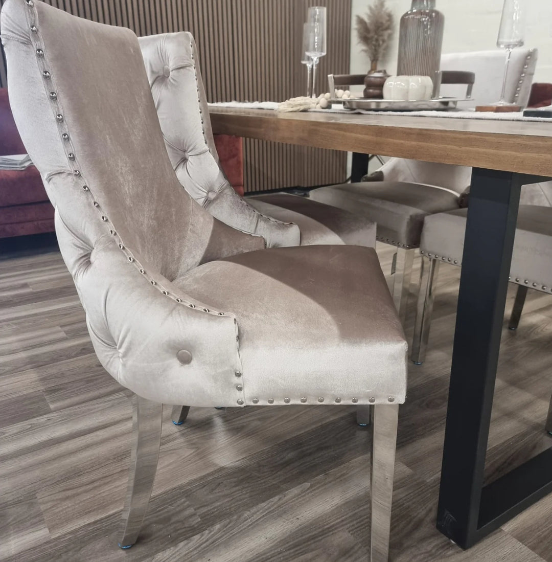 Two beige velvet Kensington dining chairs with chrome legs and deep buttoned back design, pictured in a room setting with a wooden dining table.