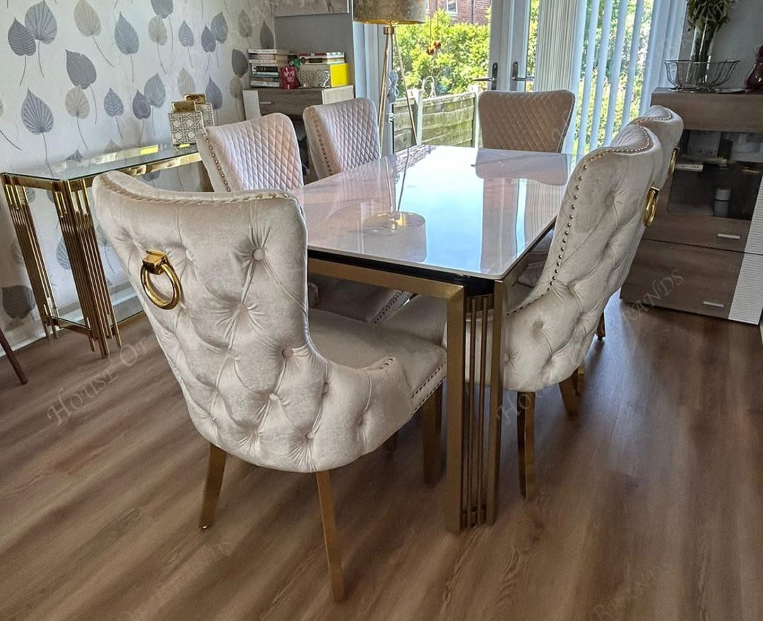 A white marble dining table with gold legs, accompanied by beige upholstered dining chairs with gold accents.