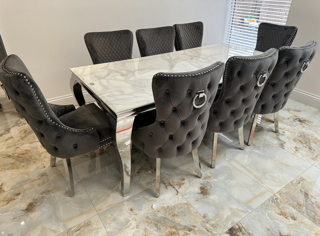 A set of dining furniture featuring a rectangular marble tabletop with a dark grey, textured pattern, surrounded by eight upholstered chairs with a tufted back design and dark frame.