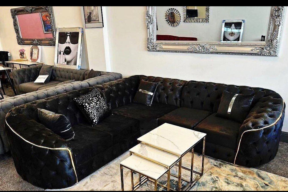 A large black corner sofa with gold accents, arranged in a showroom setting with decorative cushions and a coffee table in the foreground.