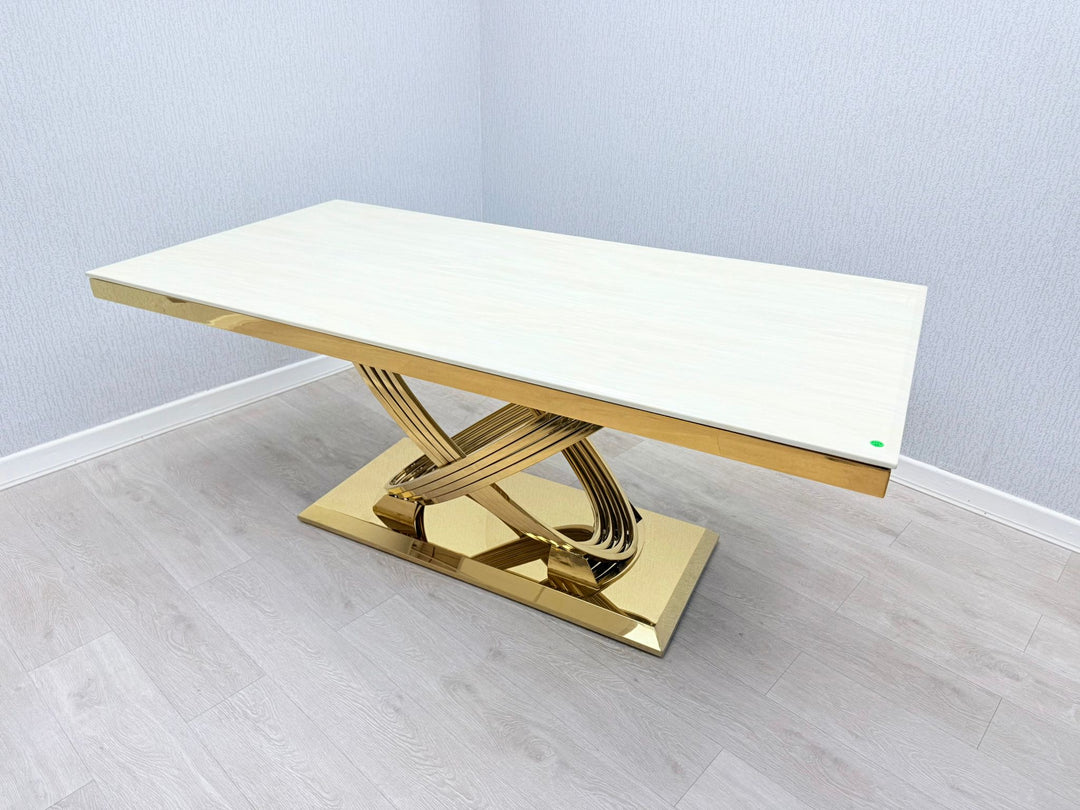 A cream and gold marble dining table with an X-shaped gold leg support, set against a plain background.