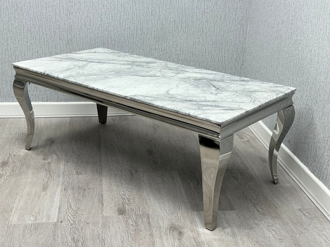 A grey marble top coffee table with silver metal legs, placed on a wooden floor against a plain wall.