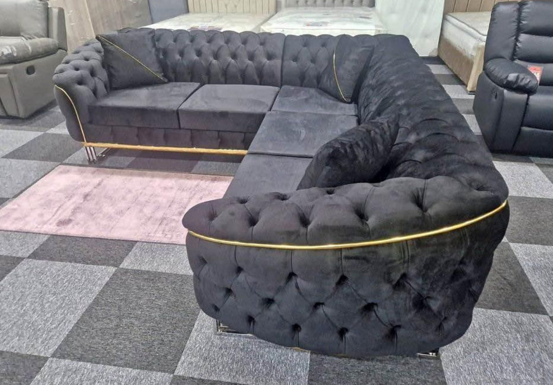 A large black corner sofa with gold accents, arranged in a showroom setting with decorative cushions and a coffee table in the foreground.