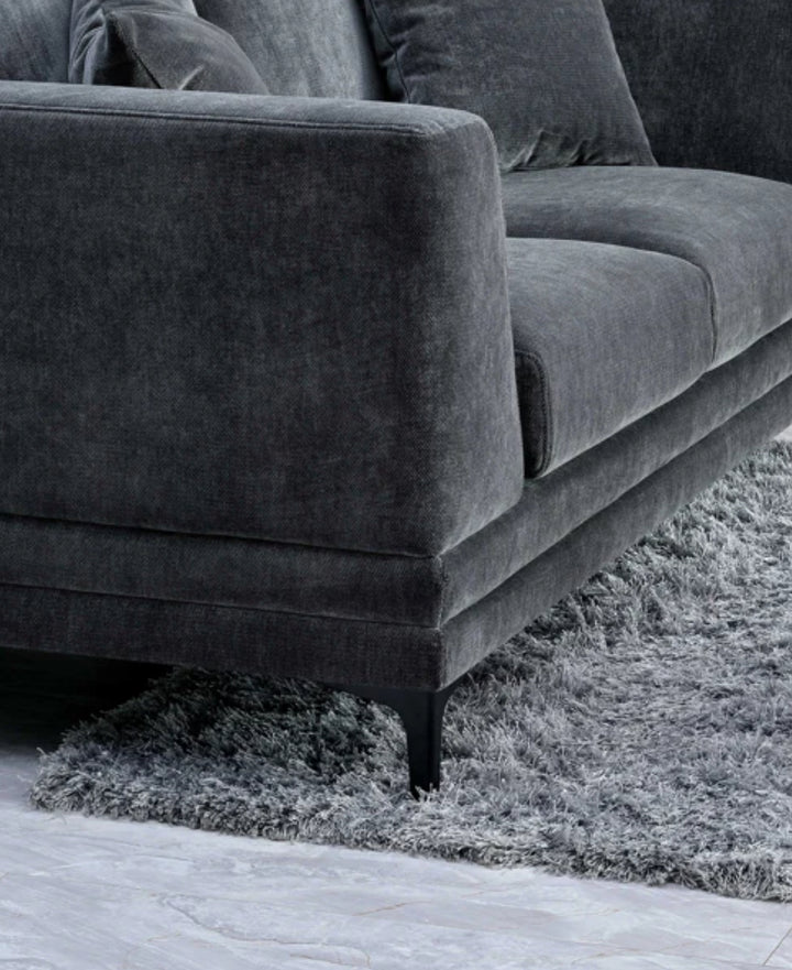 Close-up of dark grey velvet sofa armrest with plush cushions and black metal legs on a soft grey shaggy rug