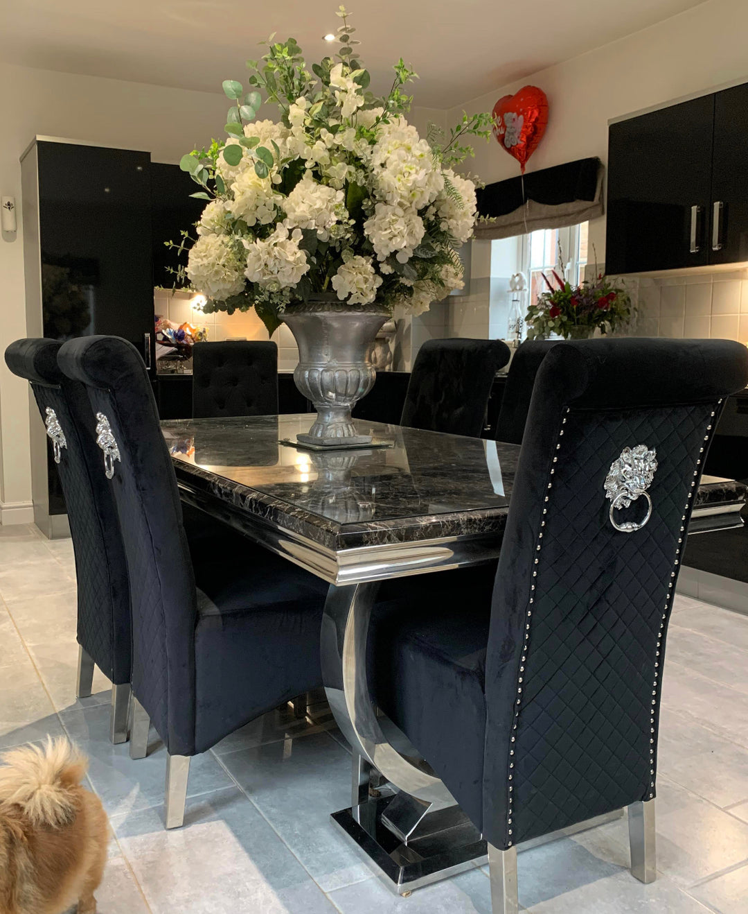 A black dining set with a marble top and steel chrome legs, including a flower vase and decorative knocker, set in a stylishly furnished dining room.