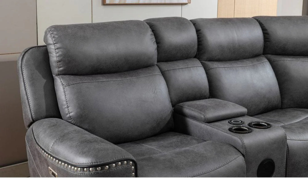 A gray fabric corner recliner sofa with multiple seats and an electronic control panel, situated in a room with a light-colored wall and a potted plant in the background.