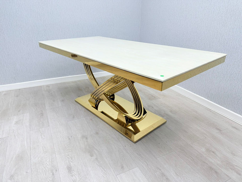 A cream and gold marble dining table with an X-shaped gold leg support, set against a plain background.