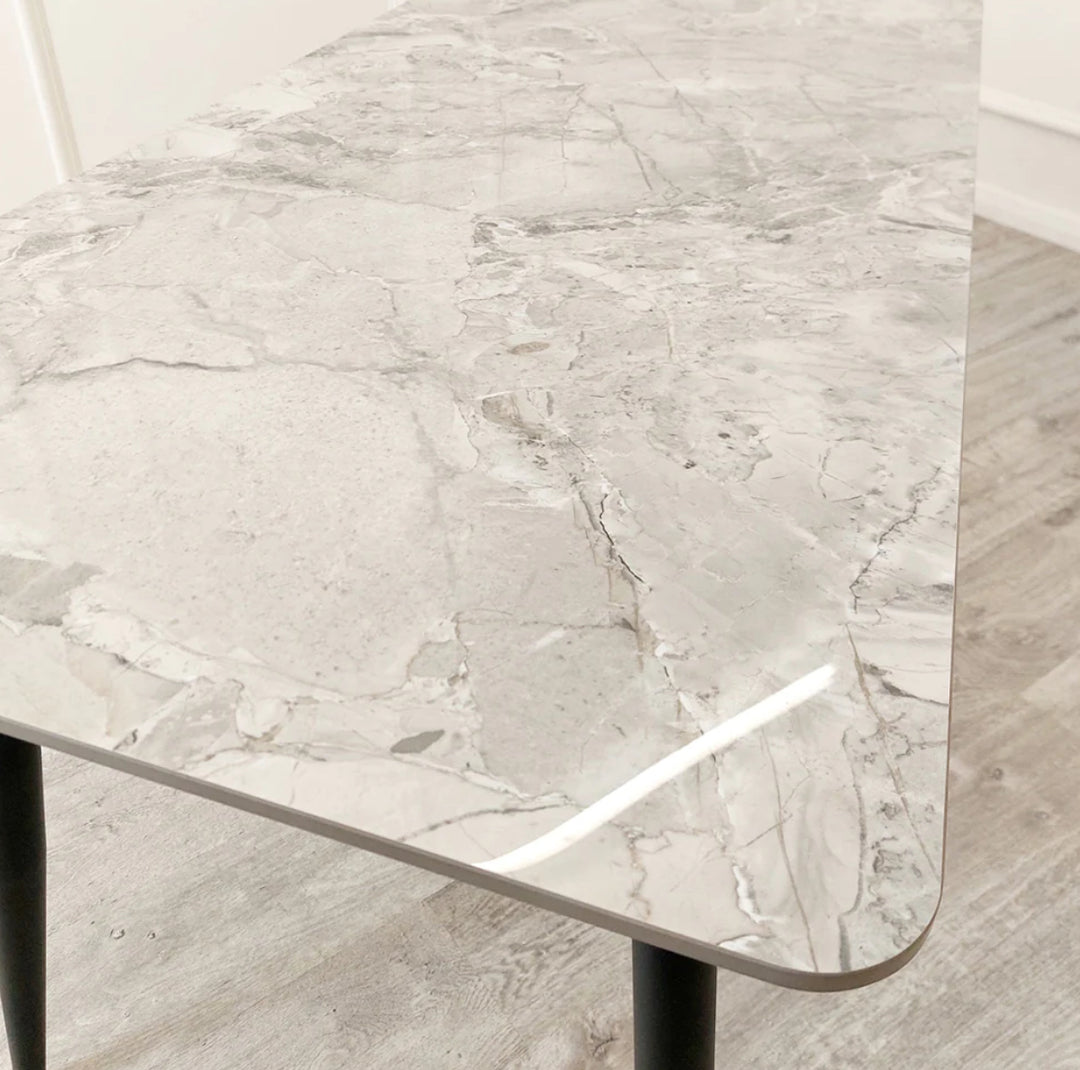 A black dining table with a grey sintered stone top and black tapered legs.