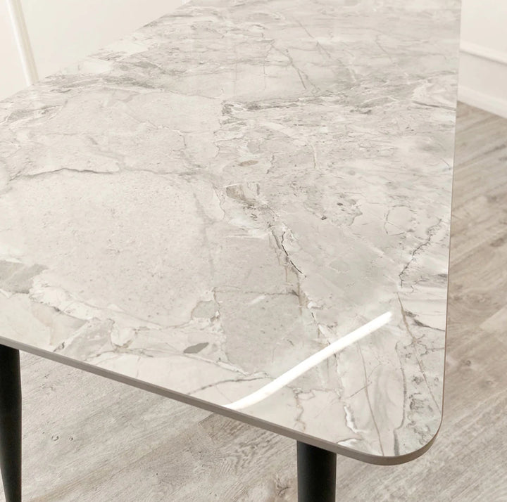 A black dining table with a grey sintered stone top and black tapered legs.