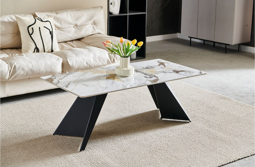 A modern white marble coffee table with a black metal frame, positioned on a beige carpet with a vase of tulips on top and a decorative pillow in the background.