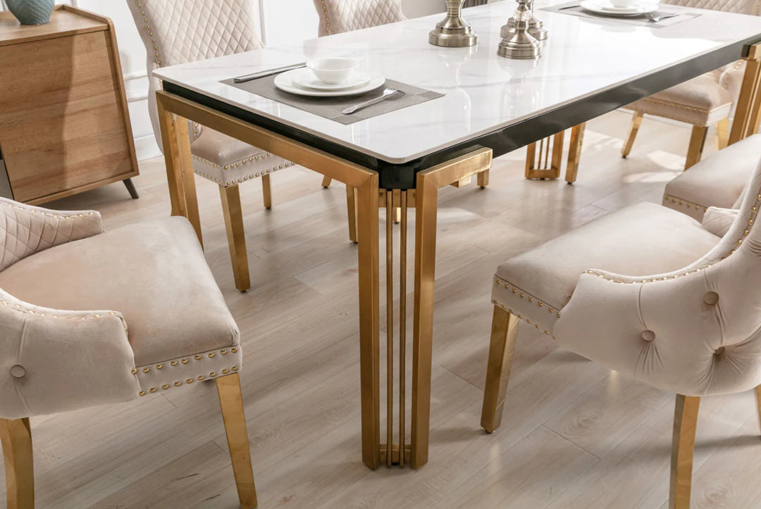 A white marble dining table with gold legs, accompanied by beige upholstered dining chairs with gold accents.