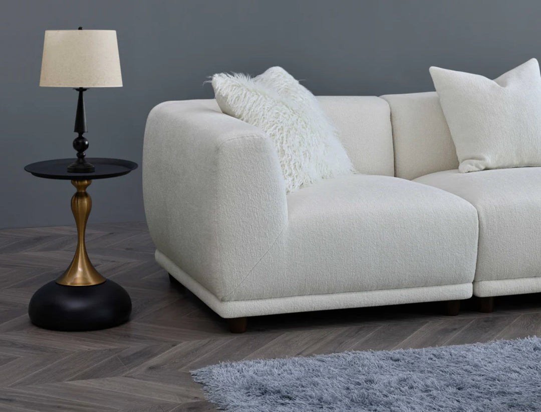A white modular corner sofa with multiple cushions in a living room setting, complemented by a wooden frame and a plush grey rug.