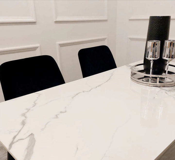 A black dining table with a white sintered stone top, featuring a minimalist design with tapered legs.
