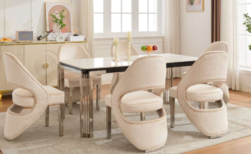 A white marble dining table with four cream plush velvet chairs arranged around it in a dining room setting.