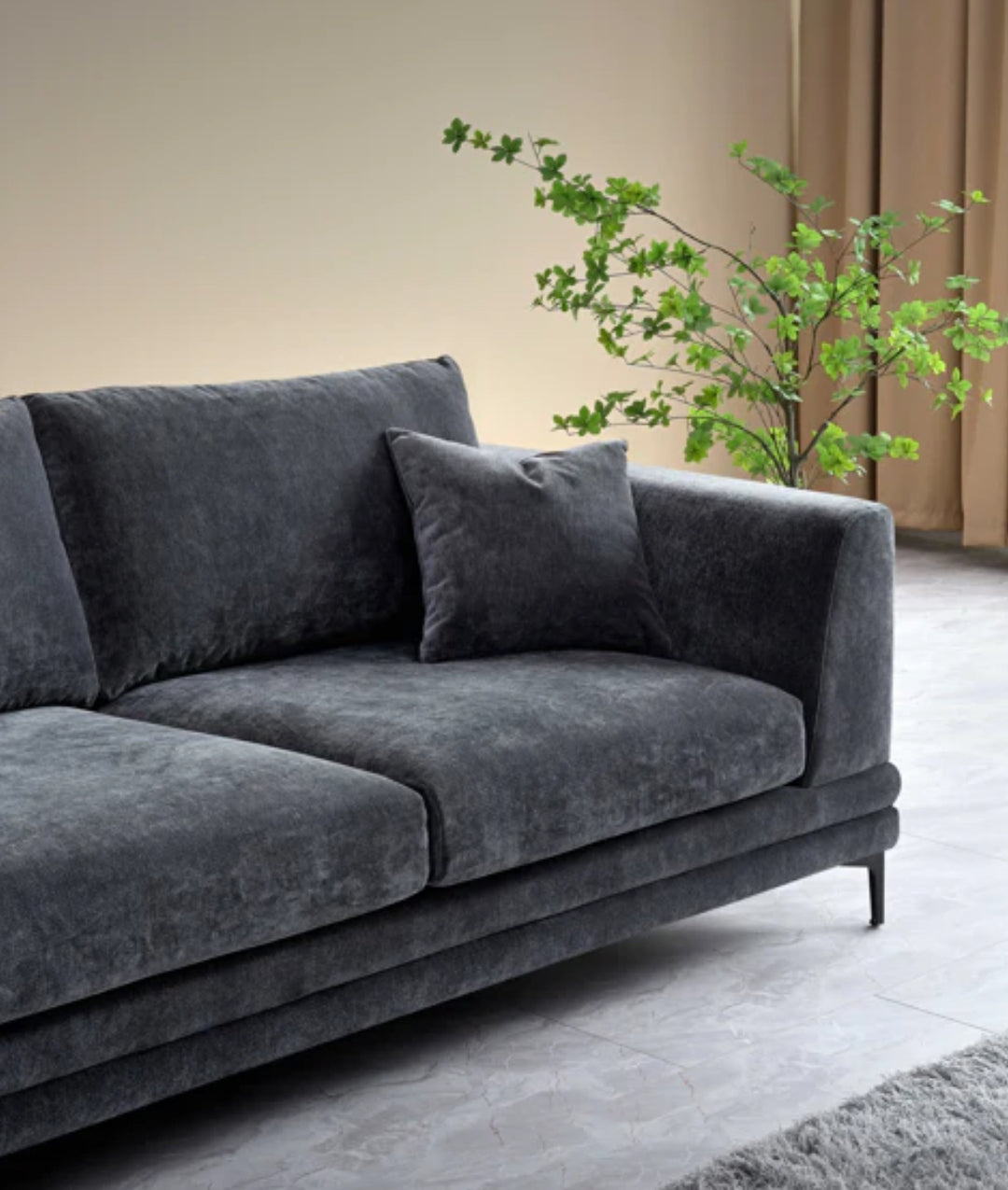 Close-up of dark grey velvet sofa armrest with plush cushions and black metal legs on a soft grey shaggy rug