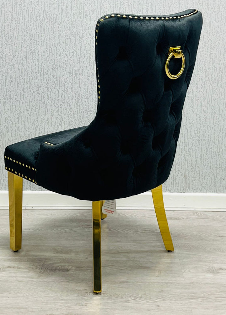 A black upholstered dining chair with gold ring knocker and legs, against a plain background.