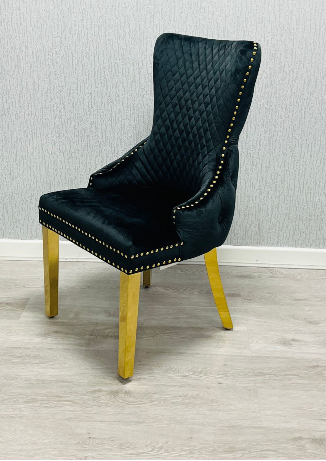 Black upholstered chair with gold legs on a light wood floor.